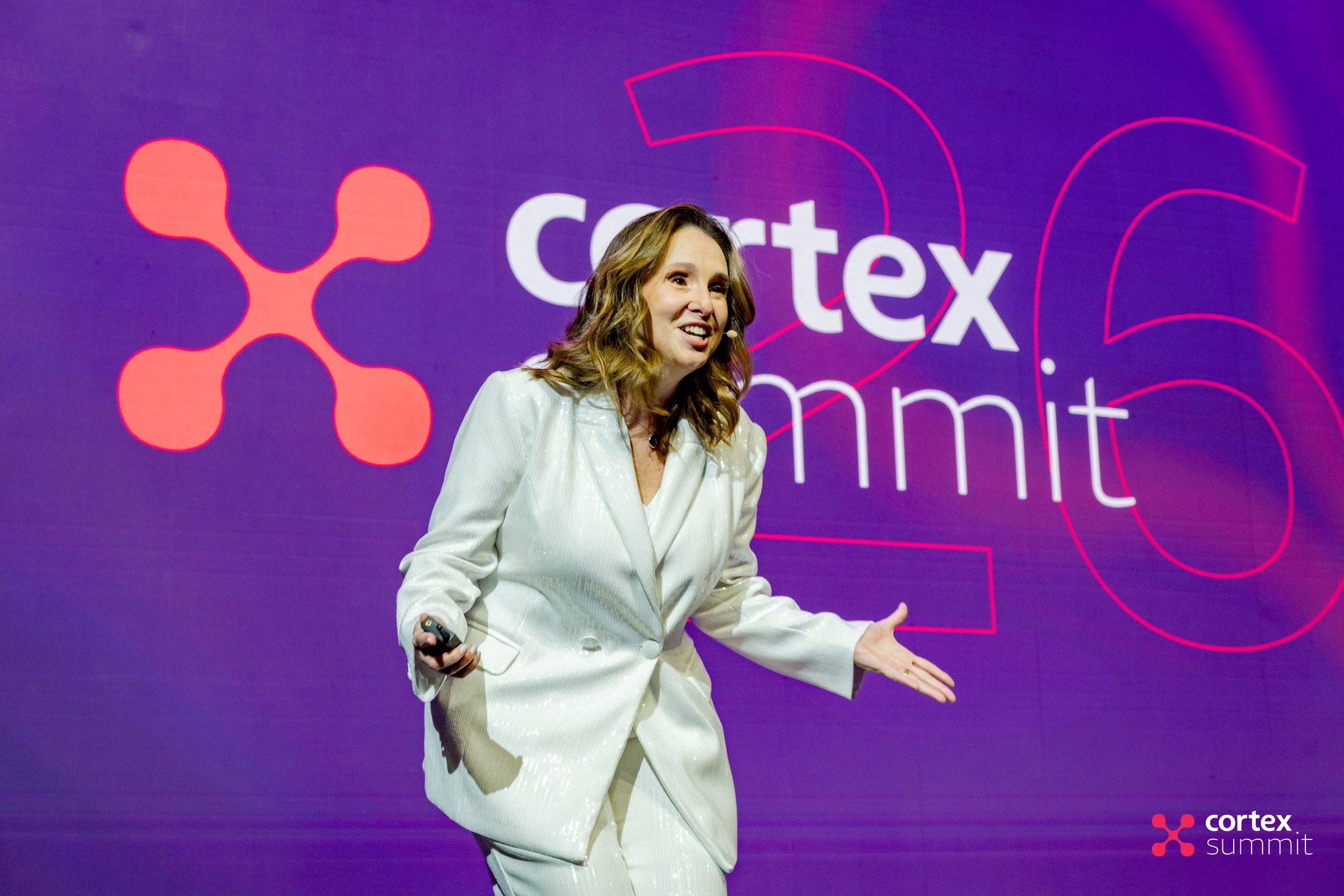 Host on stage in front of an LED wall showing the Cortex Summit logo and an outlined 26